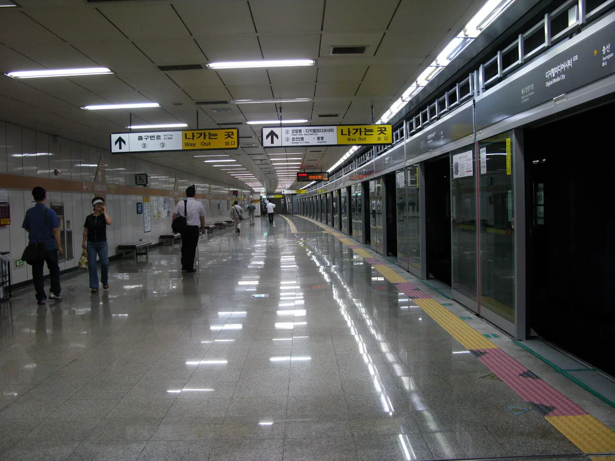 A Seoul subway platform with bilingual signage and a small number of passengers walking toward the exit.