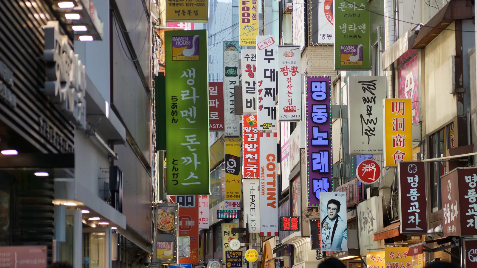 A narrow Myeongdong shopping alley in Seoul lined with dense, stacked restaurant and shop signage.