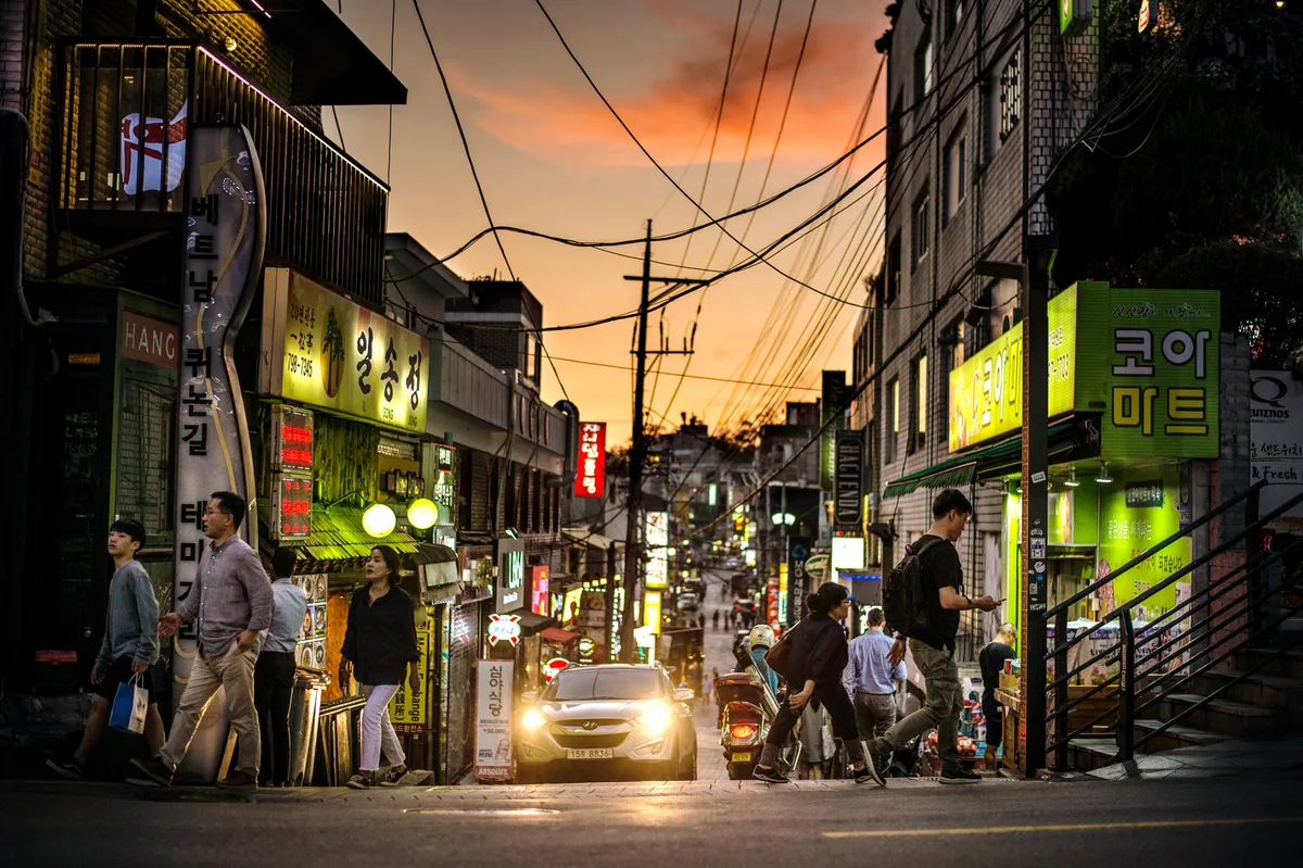 An Itaewon side street at sunset in Seoul, lined with international restaurant signage including Vietnamese and Korean shops.