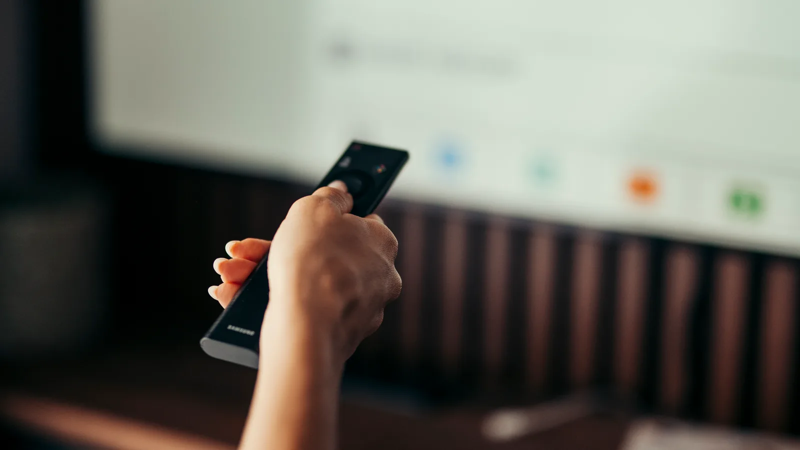 A person holding a remote control while watching television at home.