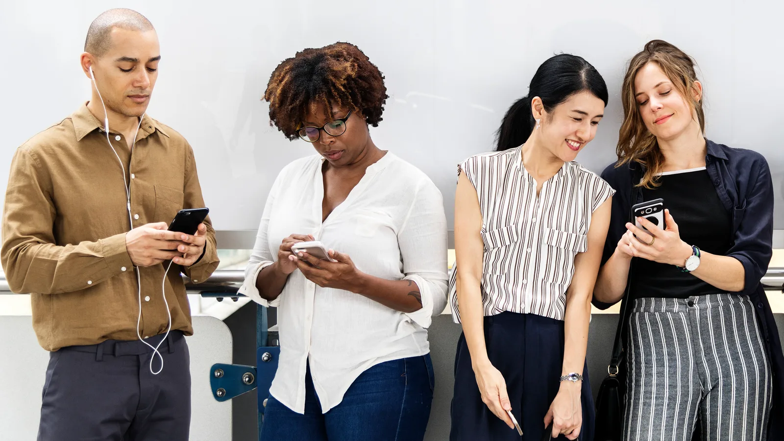 Four people standing together, each looking at a smartphone screen.