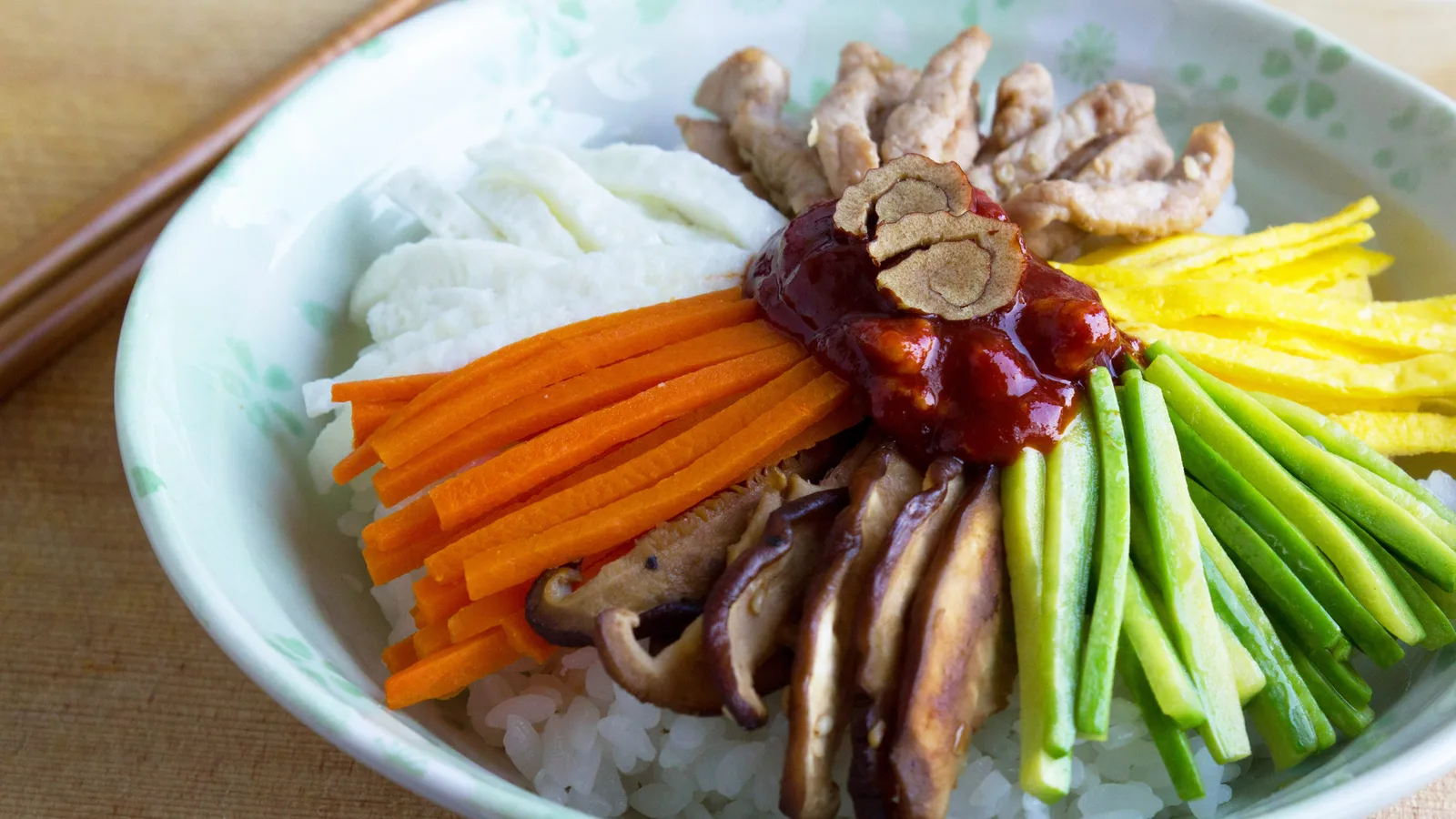 A bowl of bibimbap with rice topped by julienned vegetables, mushrooms, meat, and gochujang chili paste.