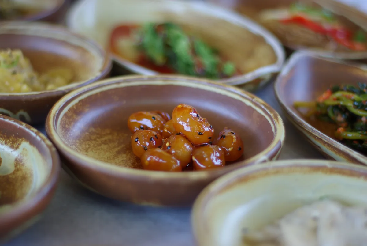 Several small banchan side dishes in individual bowls, including glazed beans, greens, and kimchi.