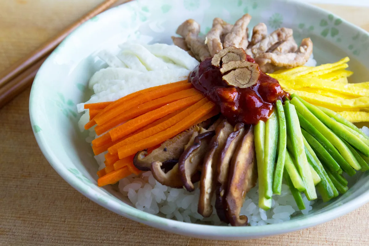 A close-up of bibimbap showing rice mixed with julienned carrot, cucumber, mushroom, egg strips, and chili paste.