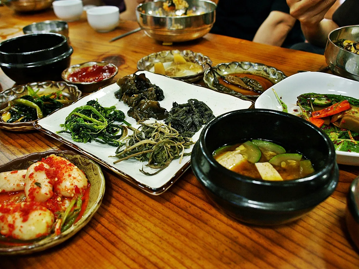 A shared Korean table setting with banchan side dishes and a pot of doenjang-jjigae at the center.