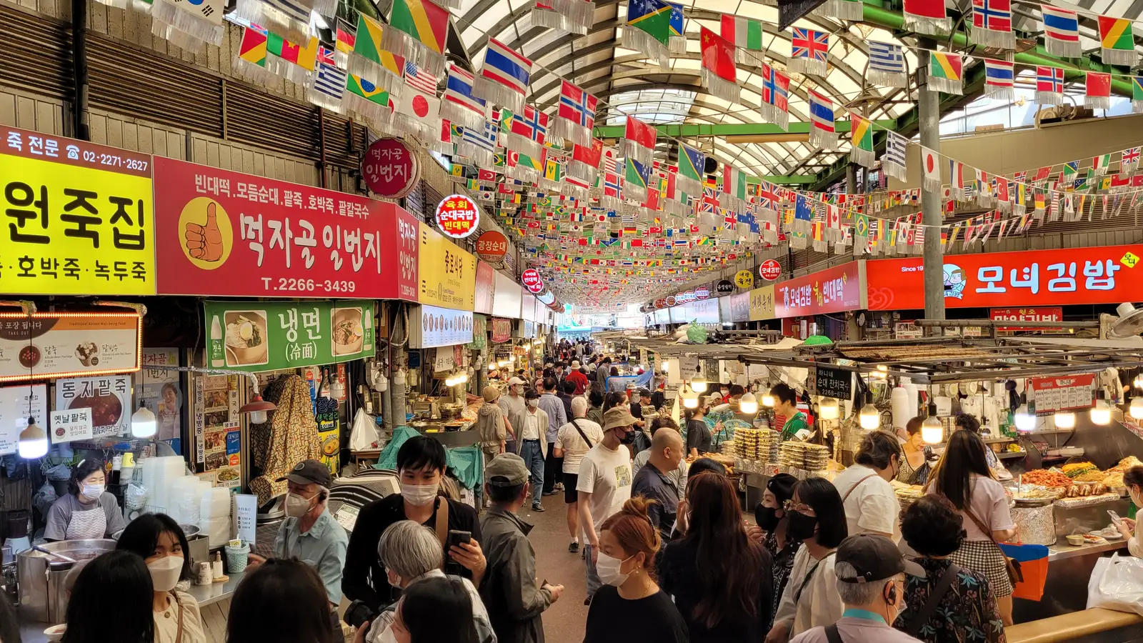 A busy aisle inside Gwangjang Market in Seoul, lined with food stalls, signage, and shoppers.