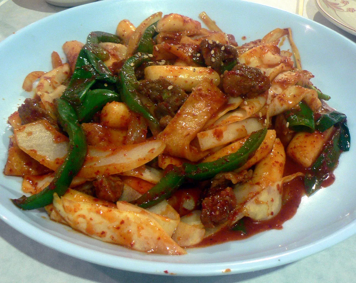 A plate of tteokbokki, rice cakes and fish cake in spicy red sauce with vegetables.