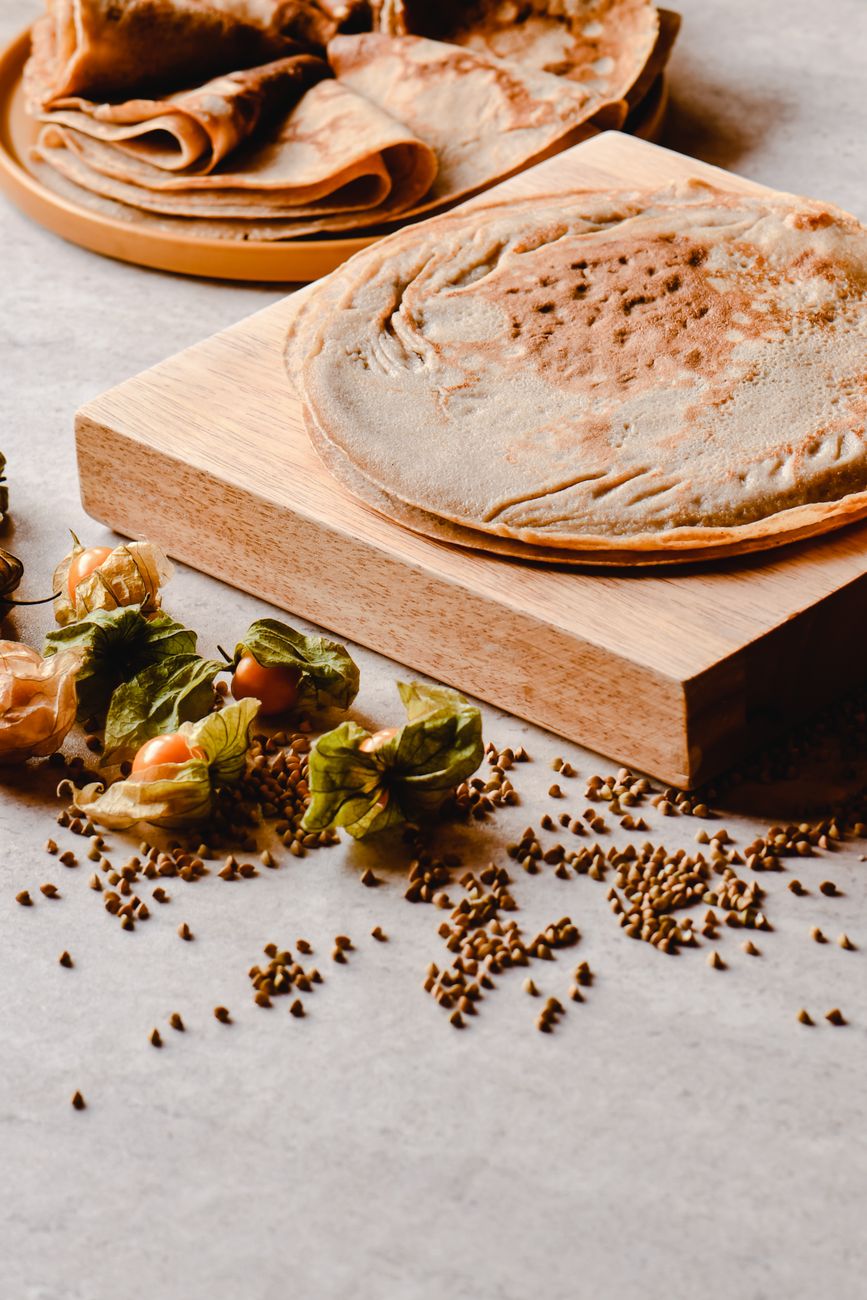 Close-up of a crepe served with buckwheat seeds and physalis, shot on a wooden board.