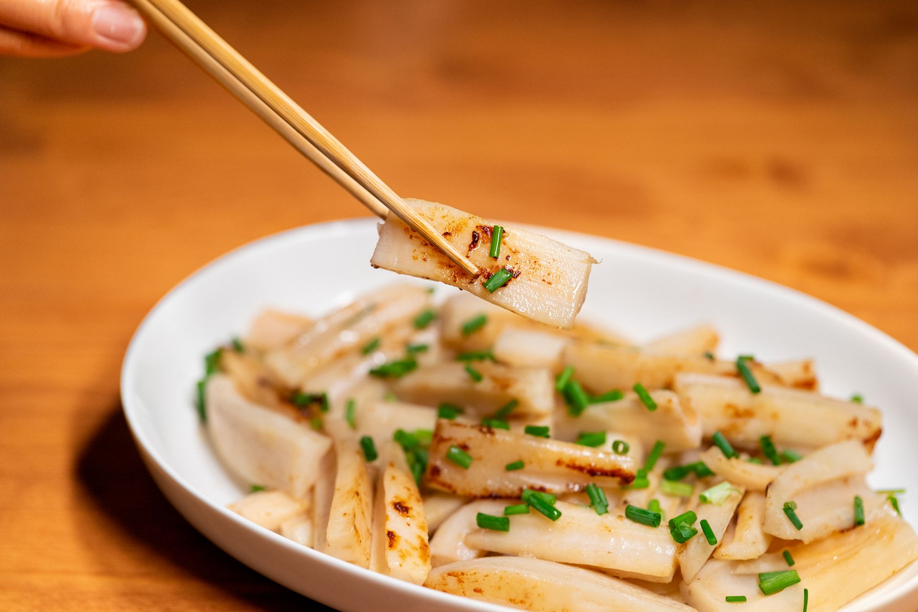 Delicious Korean rice cake dish garnished with fresh chives, captured with chopsticks.
