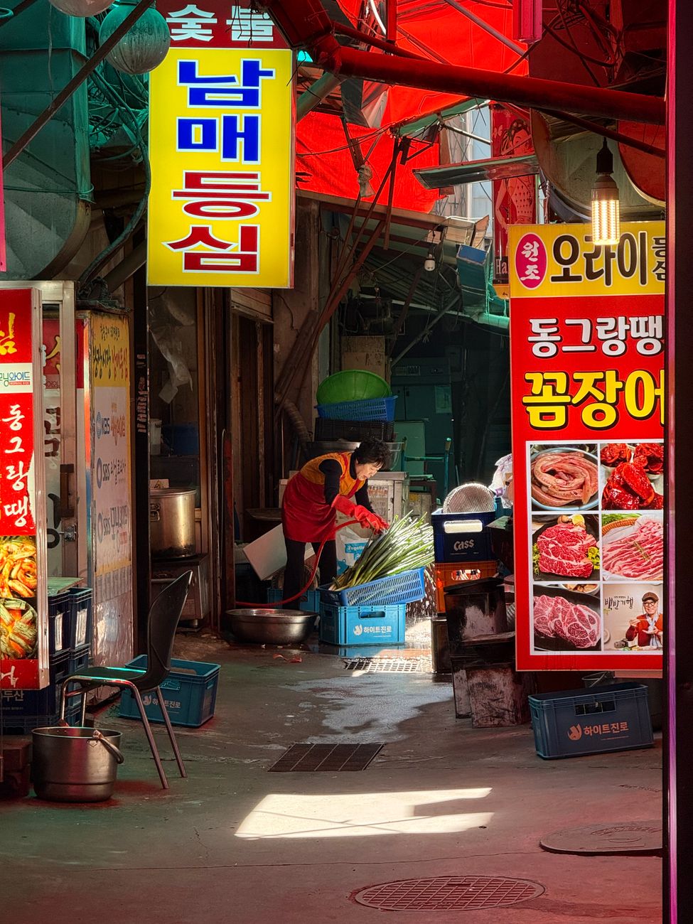 A bustling market alley in Seoul, showcasing colorful signs and a vendor preparing vegetables.