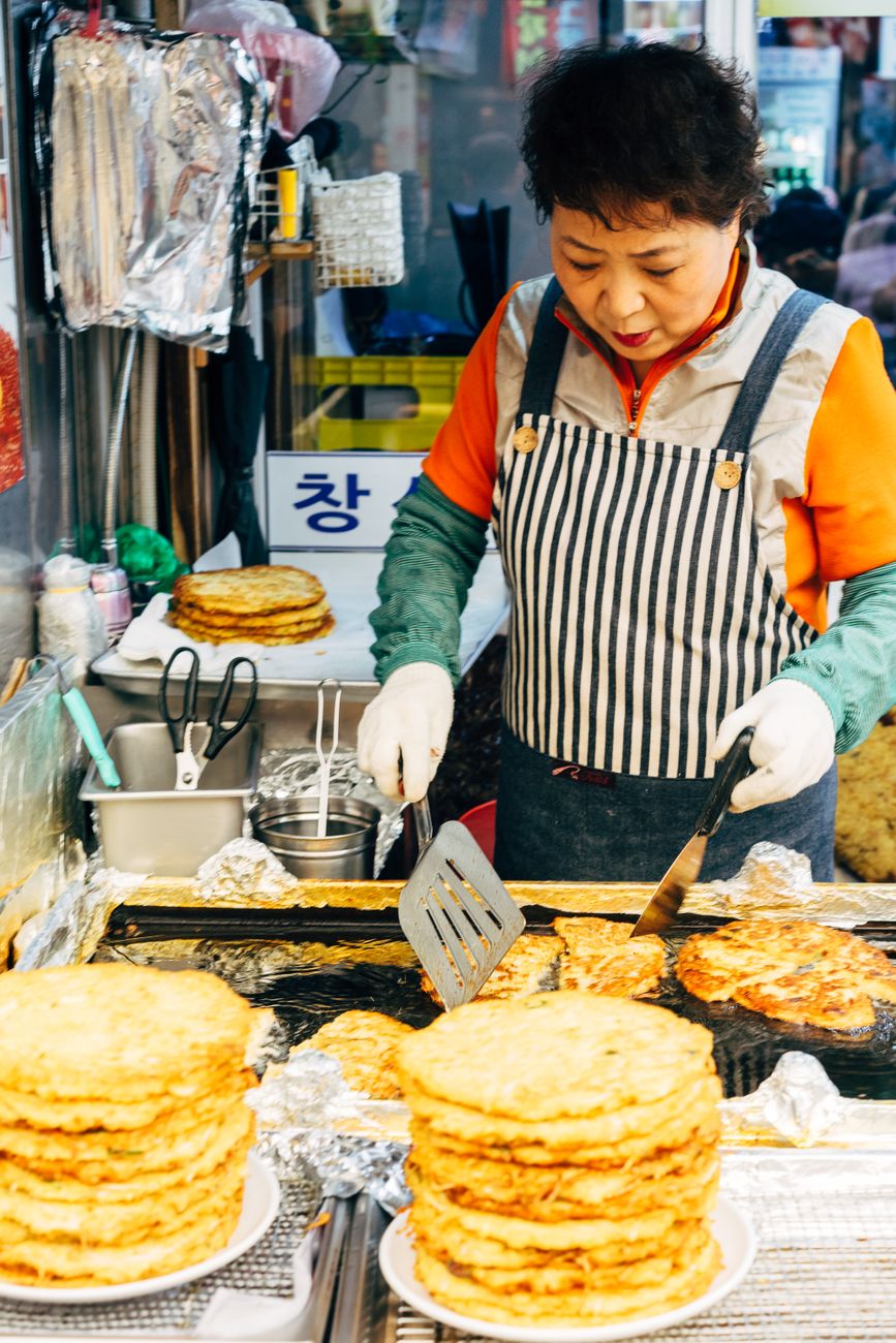 Asian woman cooking traditional pancakes at a vibrant street market stall