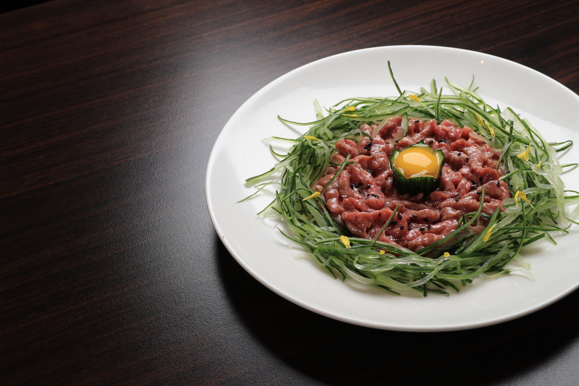 A gourmet beef tartare served with cucumber and a raw egg yolk in an elegant presentation.