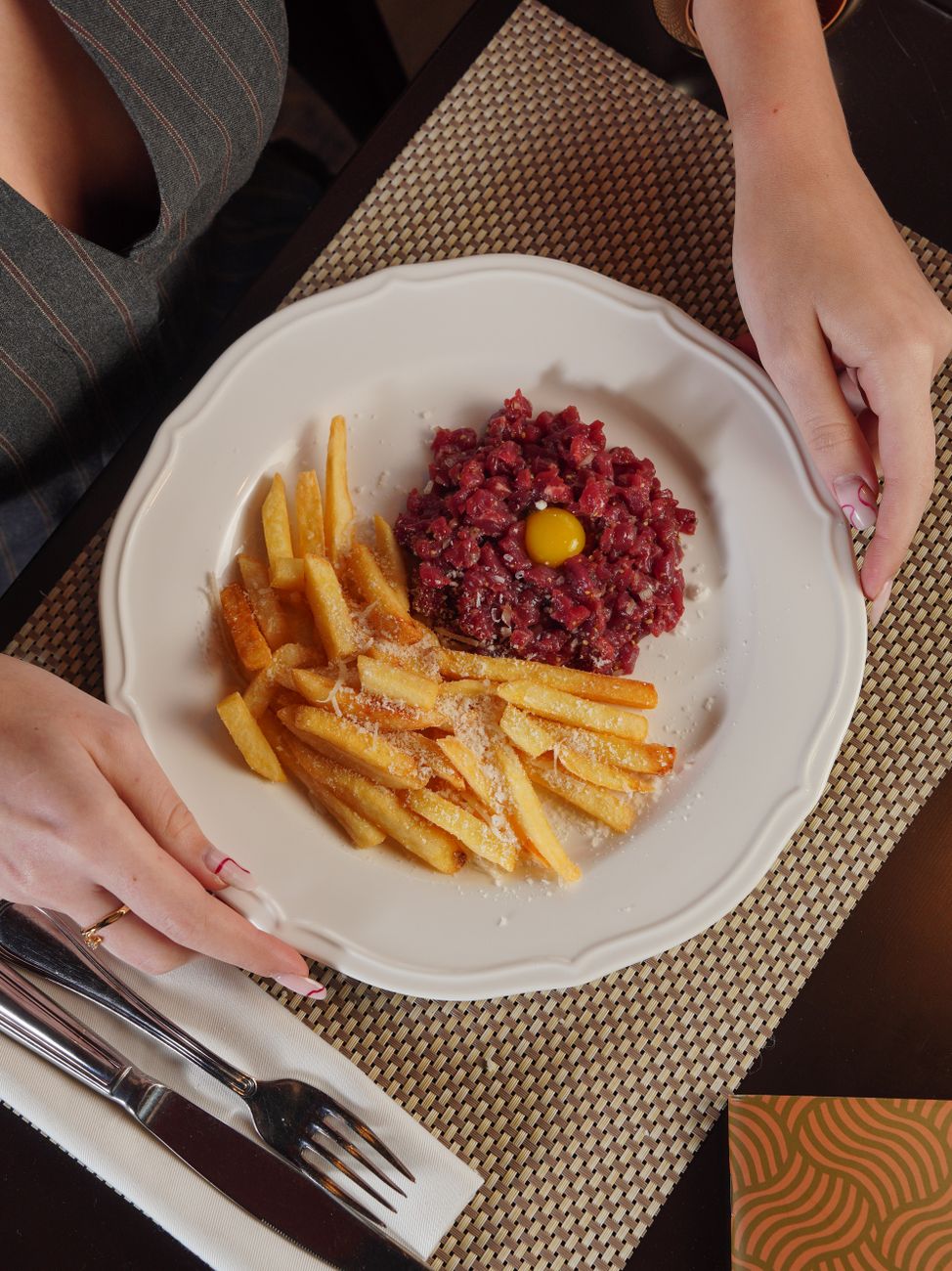 Elegant steak tartare with egg yolk and crispy fries served at a restaurant table.