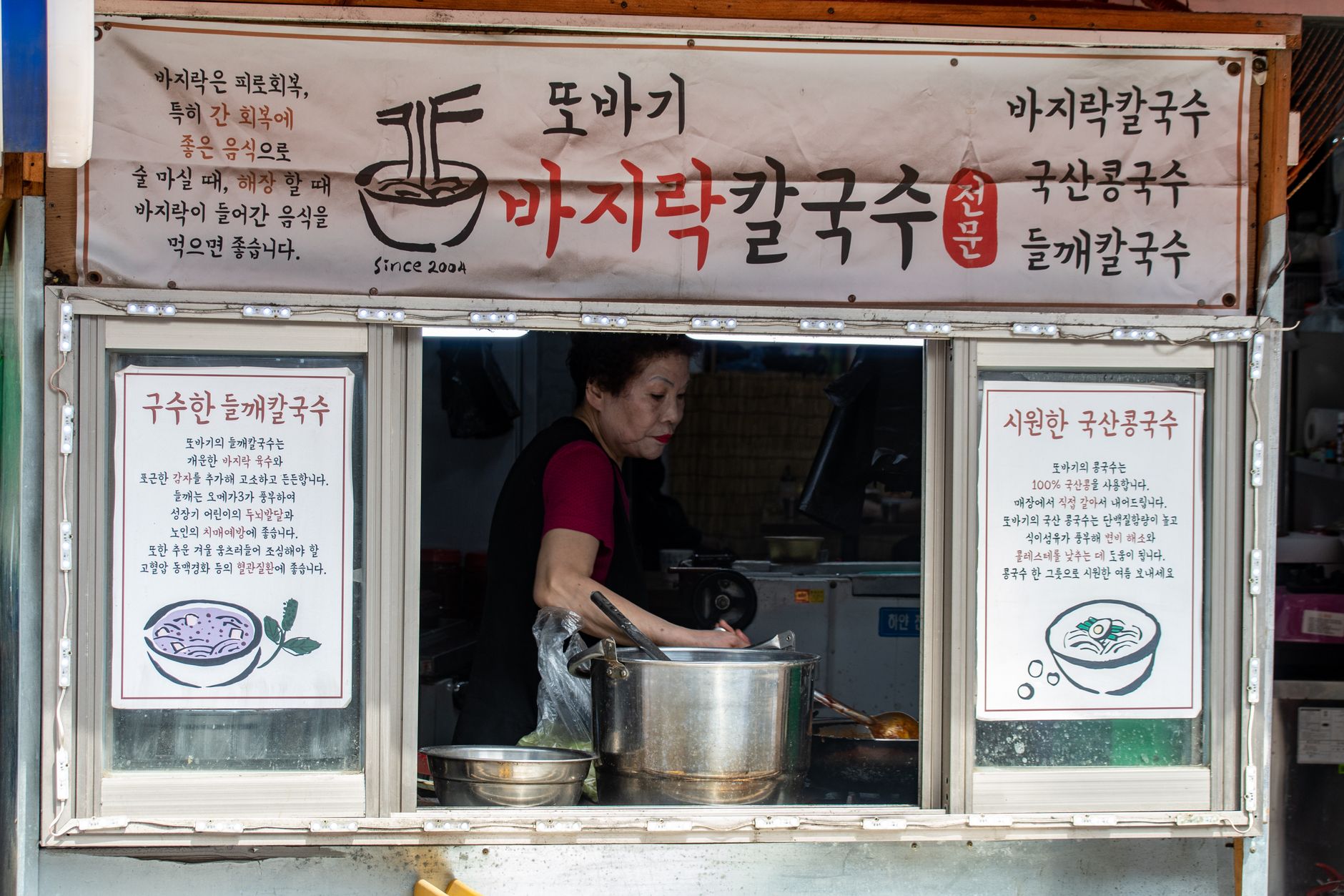 Street vendor preparing traditional Korean noodles at a food stall in Seoul's vibrant market district.