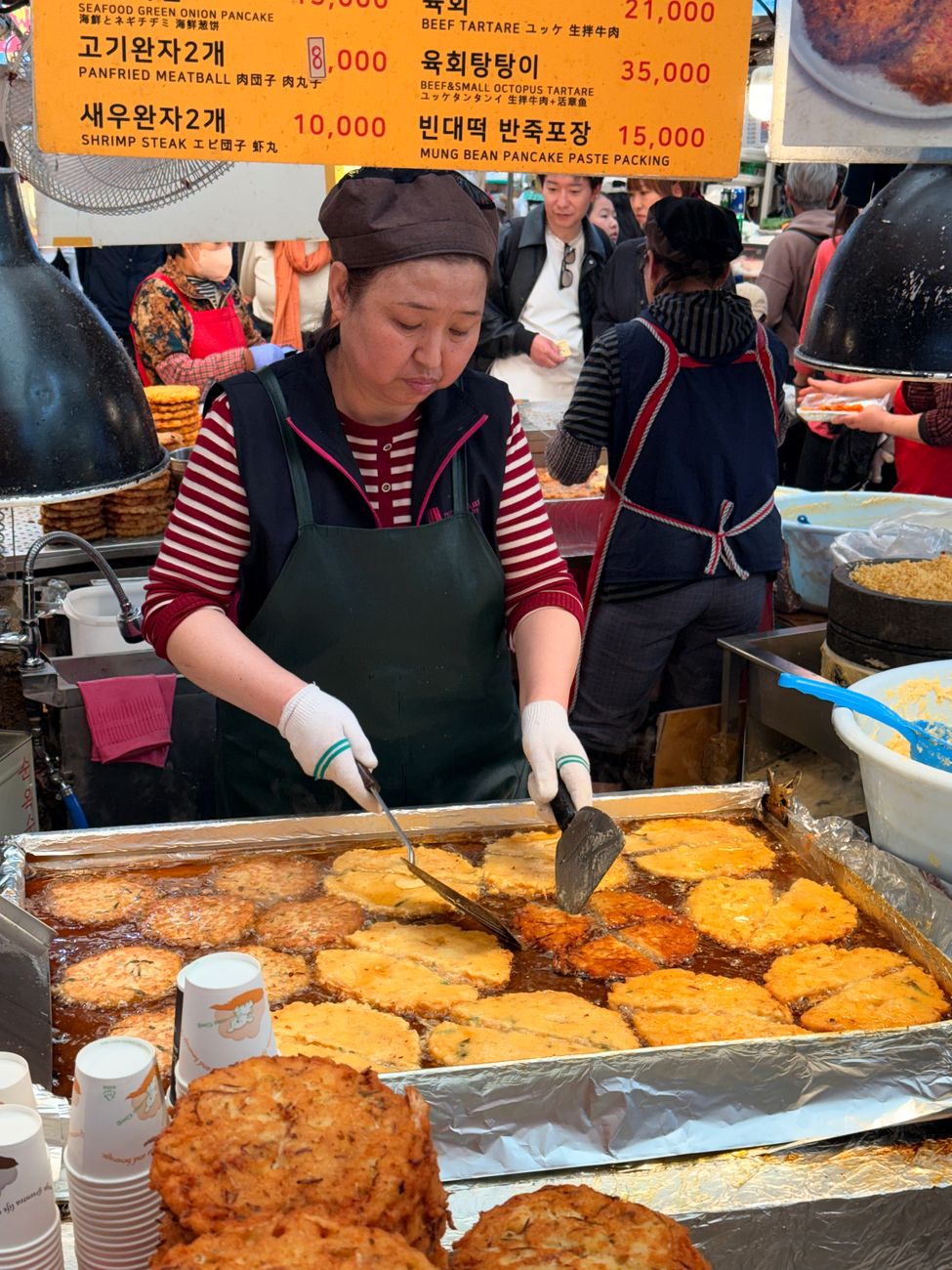 A Korean vendor prepares traditional mung bean pancakes at a bustling street market.
