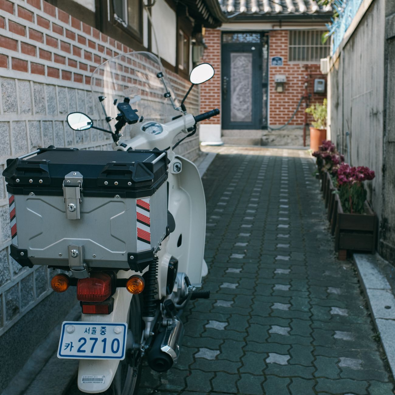 White scooter parked in a quaint narrow alley of Seoul, South Korea, beside a brick house.