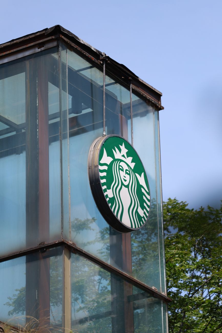 Starbucks logo sign on an outdoor glass building with clear blue sky background.
