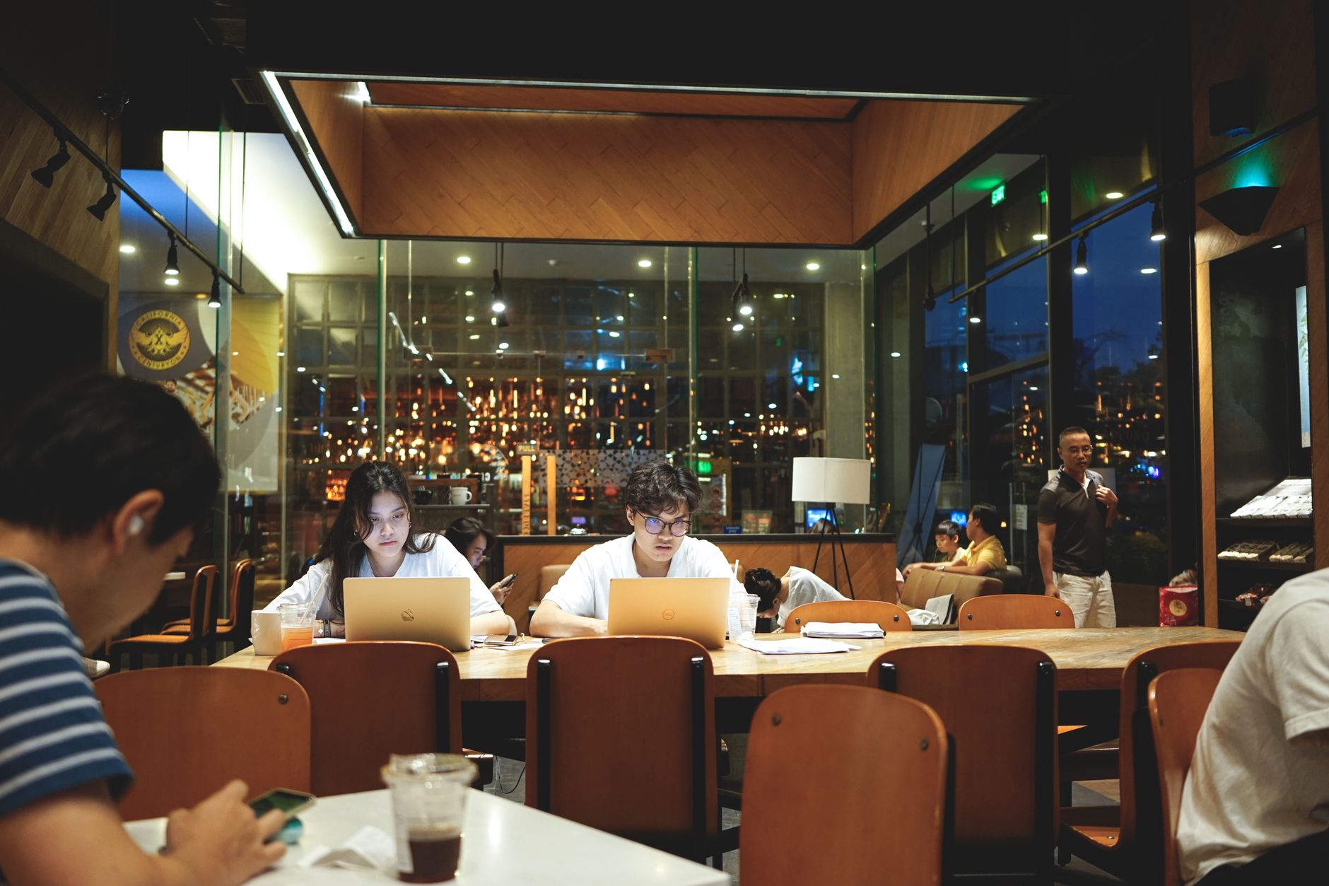People working on laptops in a busy indoor cafe with cozy lighting.