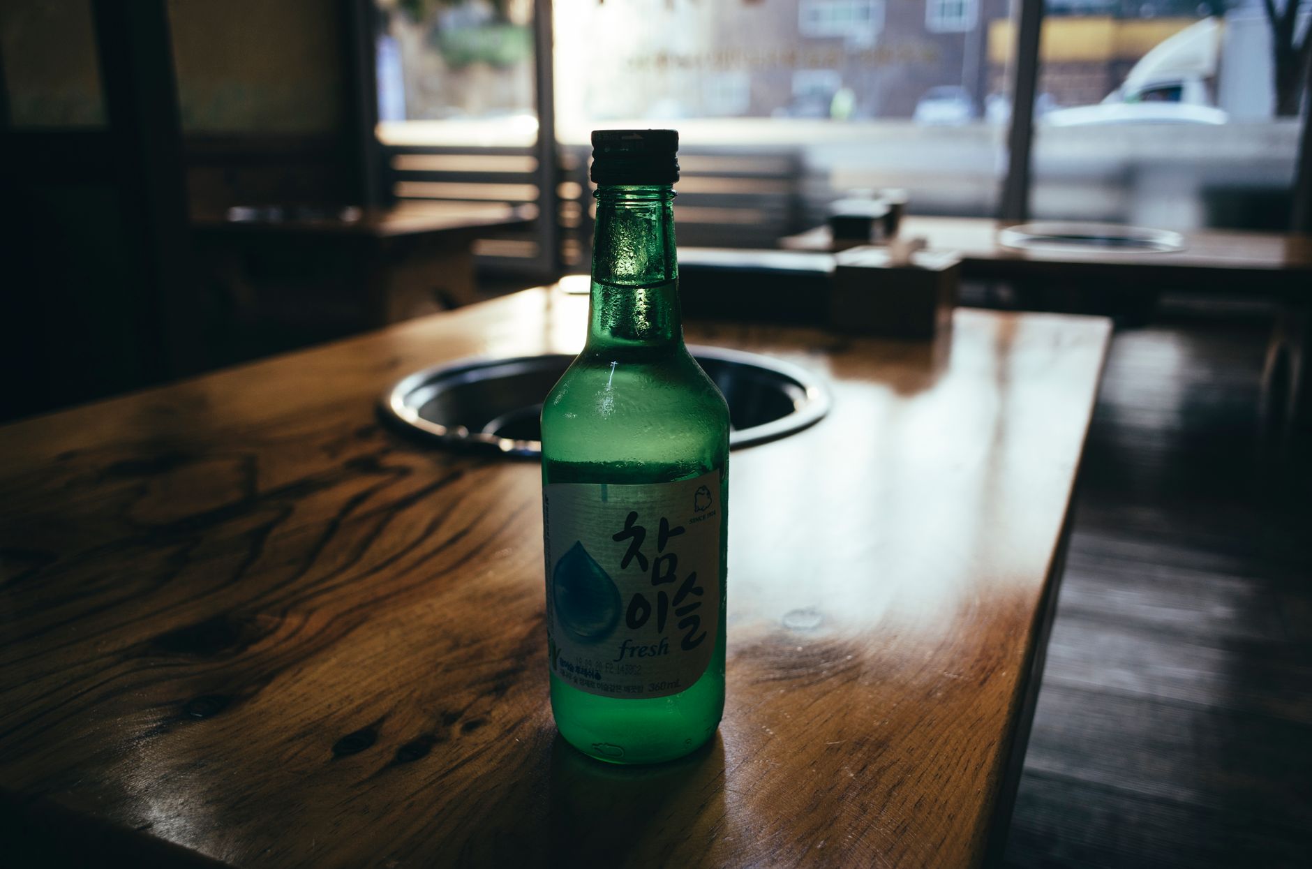 Green soju bottle on a wooden table, indoors, with natural light.