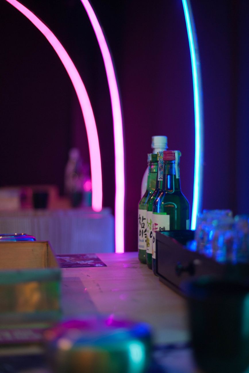 Colorful soju bottles on a bar with neon lights creating a vibrant atmosphere.