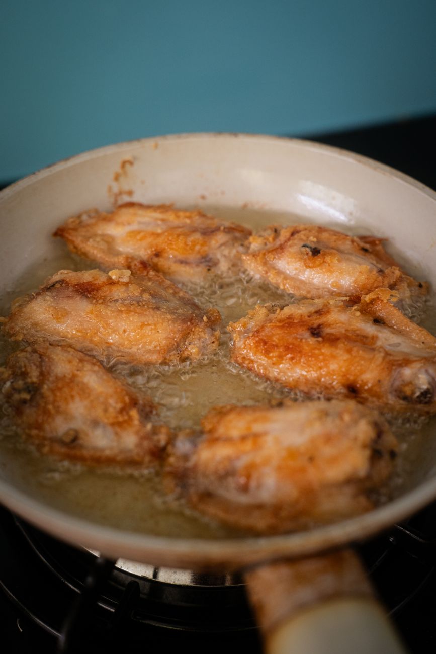 Crispy fried chicken wings sizzling in a hot pan with oil in a Vietnamese kitchen.