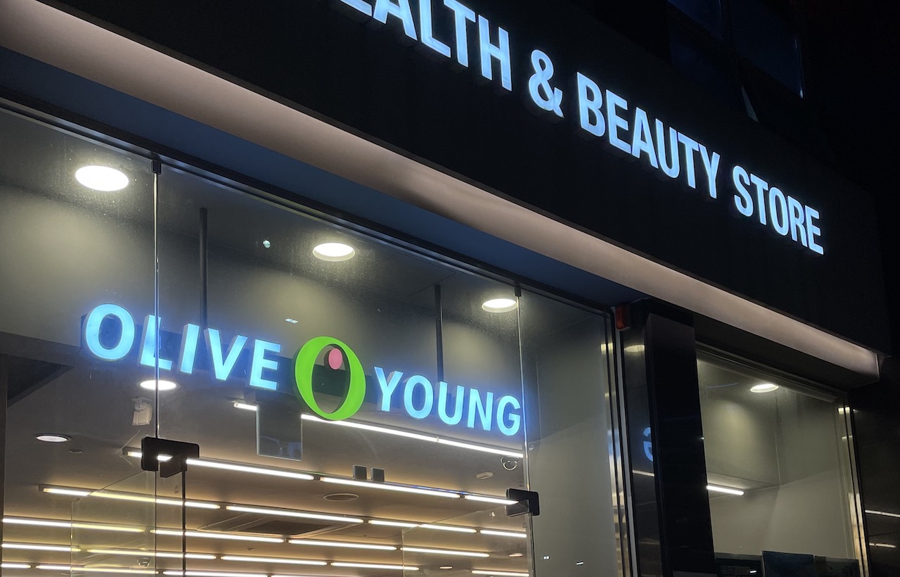 An illuminated storefront sign reading OLIVE YOUNG, HEALTH & BEAUTY STORE, at a Korean drugstore location.
