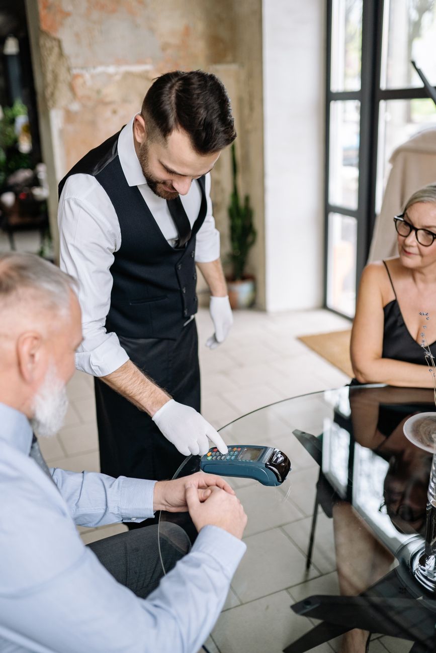 Senior couple paying with card at a restaurant, assisted by a waiter using a terminal.