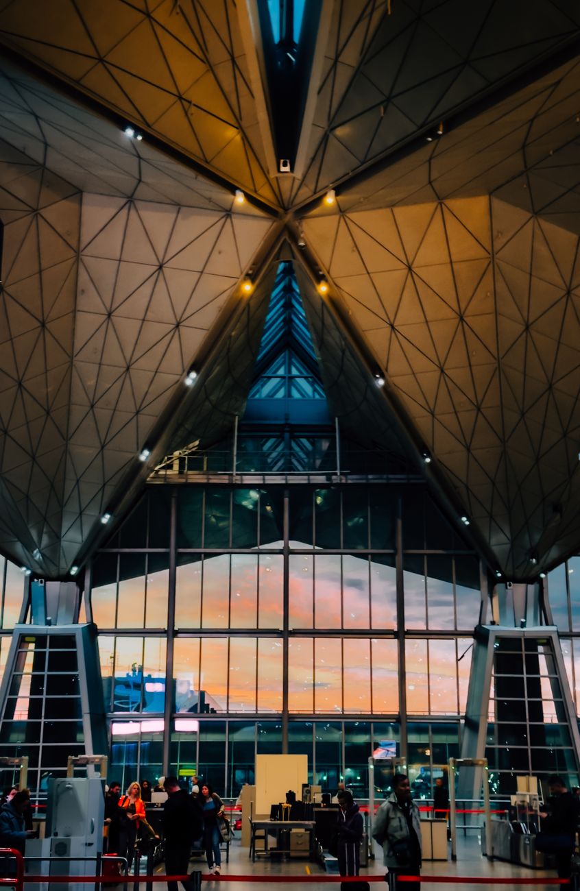 A modern airport terminal with stunning architectural design illuminated at sunset, depicting a busy scene with travelers.
