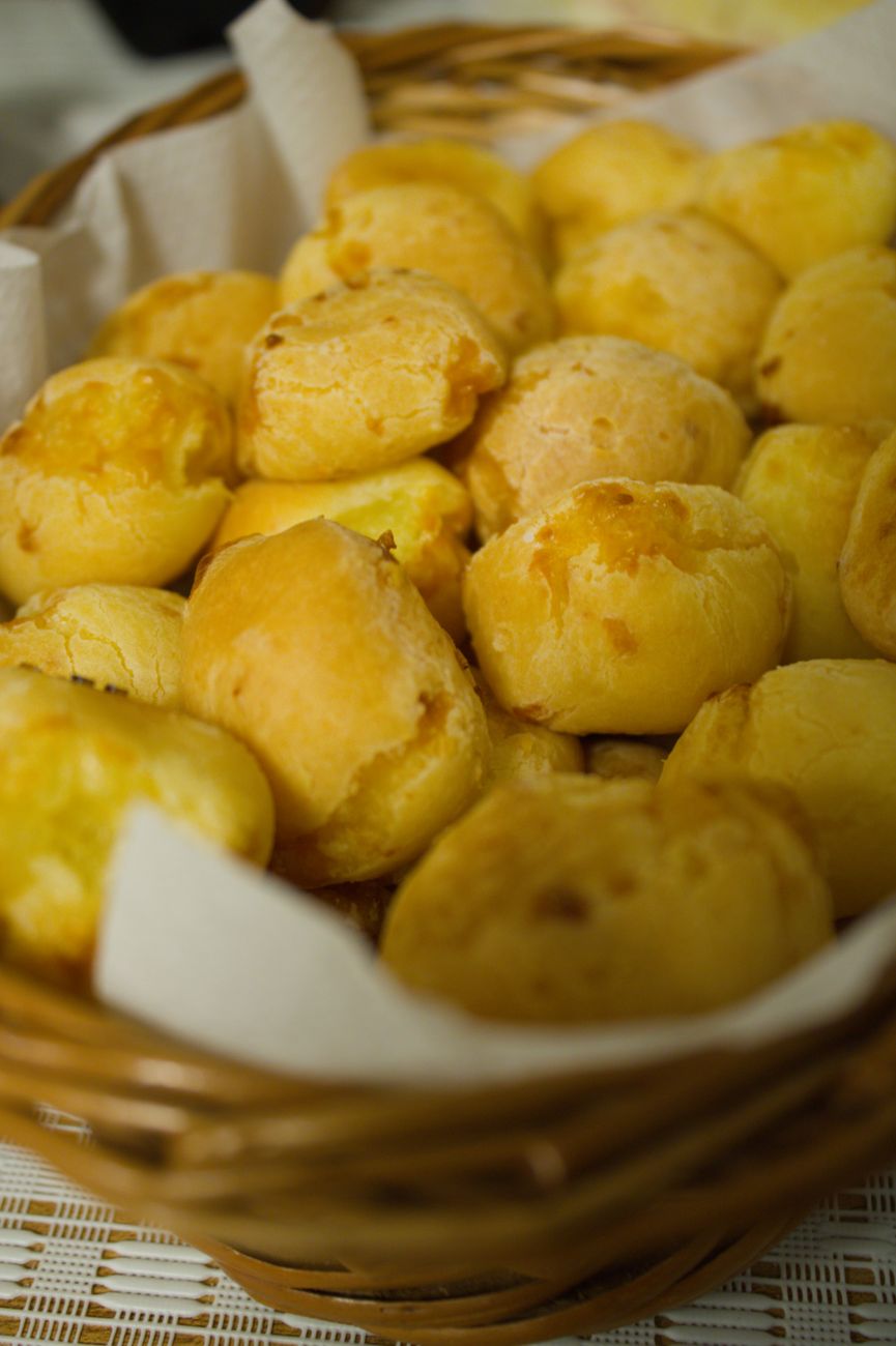 Closeup of freshly baked Brazilian cheese bread, Pão de Queijo, in a wicker basket, ideal for food blogs.