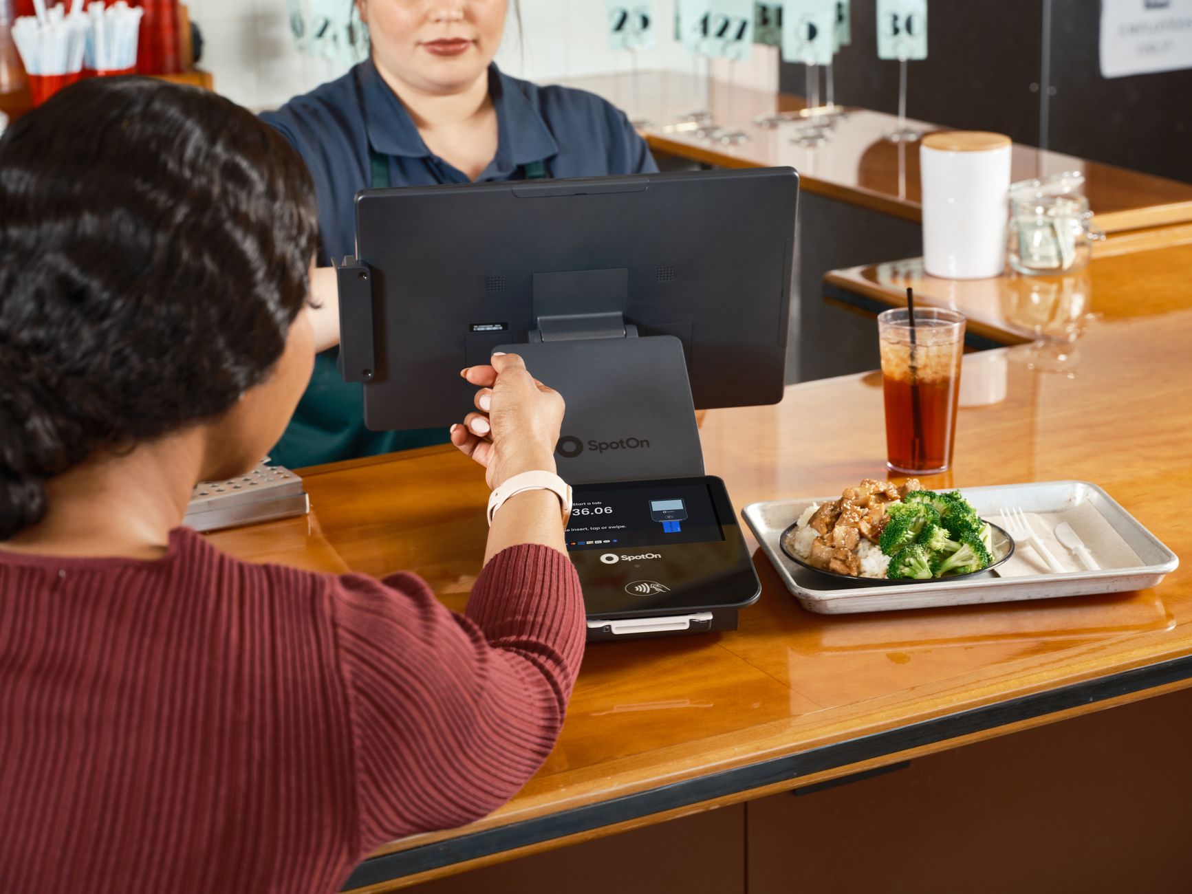 A customer uses smartwatch for contactless payment at a restaurant with SpotOn POS system.