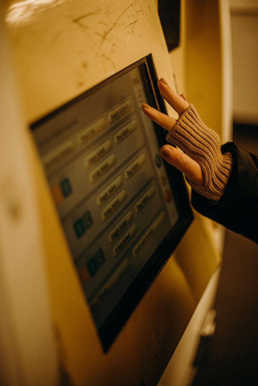 A close-up image of a gloved hand operating a Berlin U-Bahn ticket machine showing electronic interface and selection buttons.