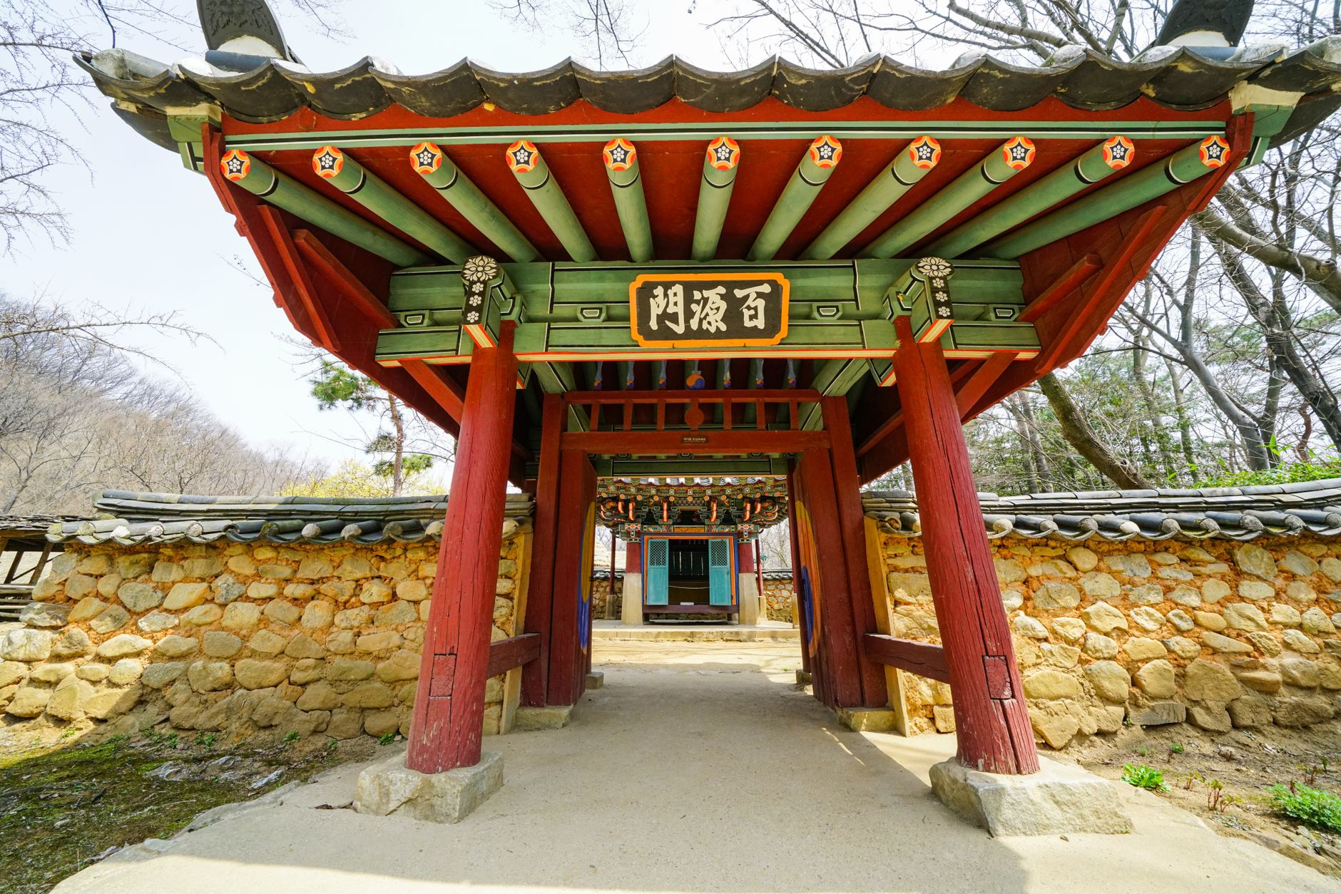 A vibrant Korean temple gate with intricate design, framed by stone walls and trees.