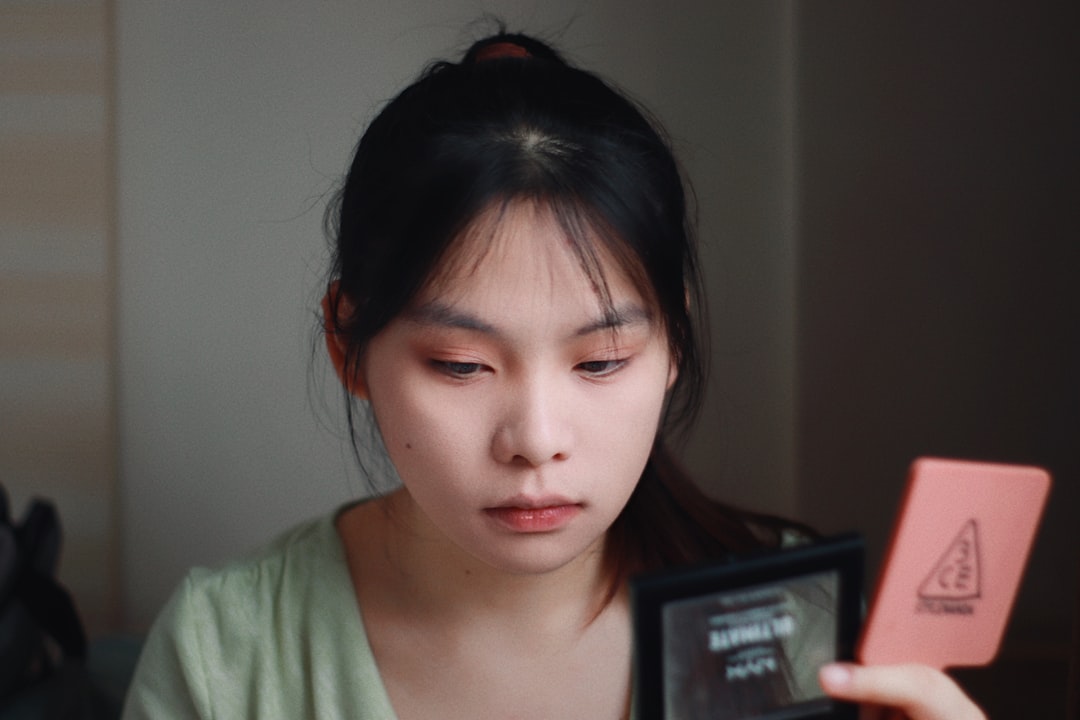 Woman applies makeup, looking in a compact mirror.