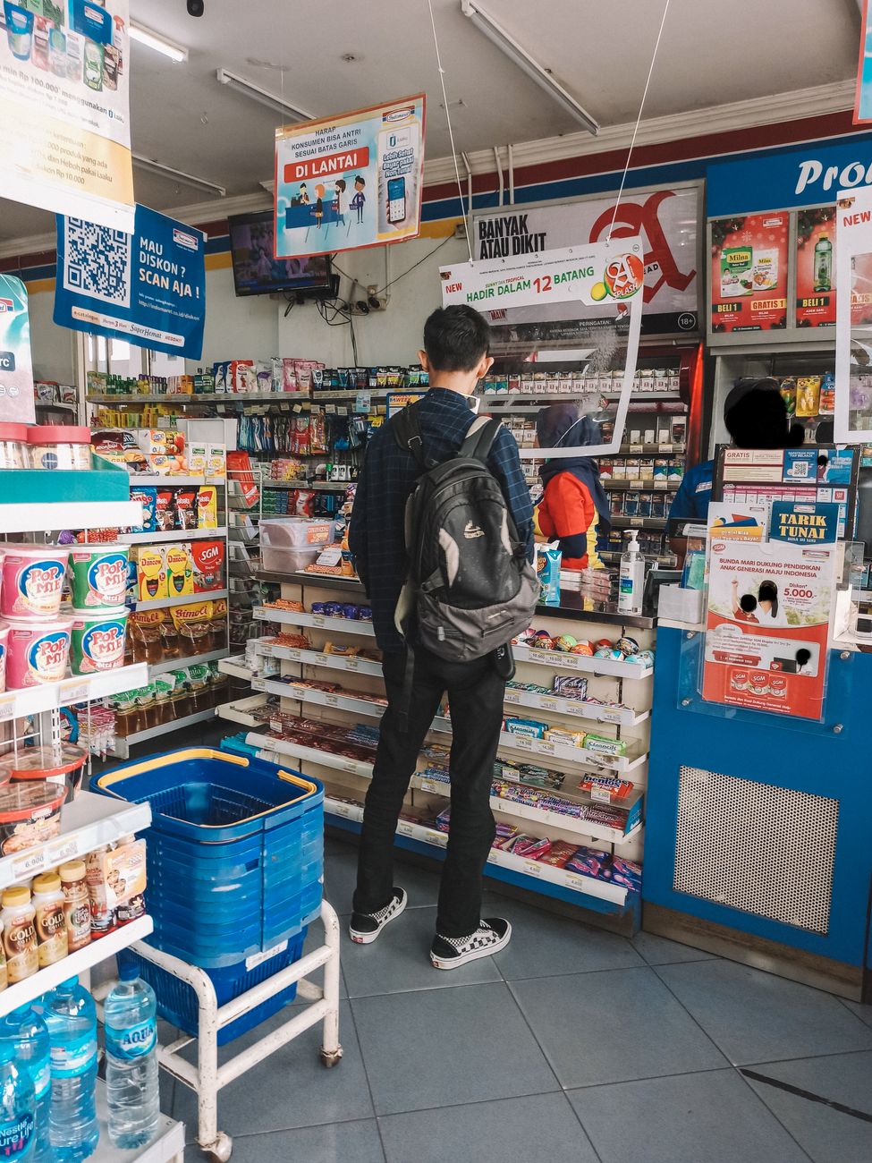 A man with a backpack shops at a convenience store counter filled with various products.