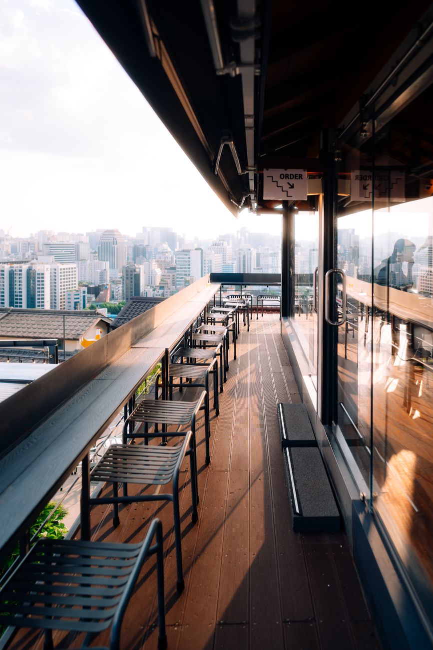 Sunlit terrace of a modern rooftop cafe with panoramic views of the Seoul skyline, South Korea.