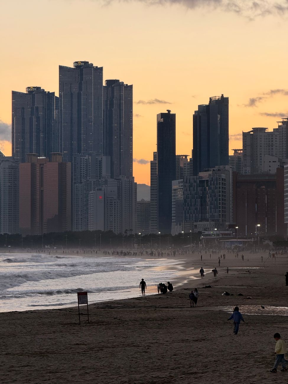 A scenic sunset view of a beach with people and skyscrapers in Haeundae, Busan, South Korea.