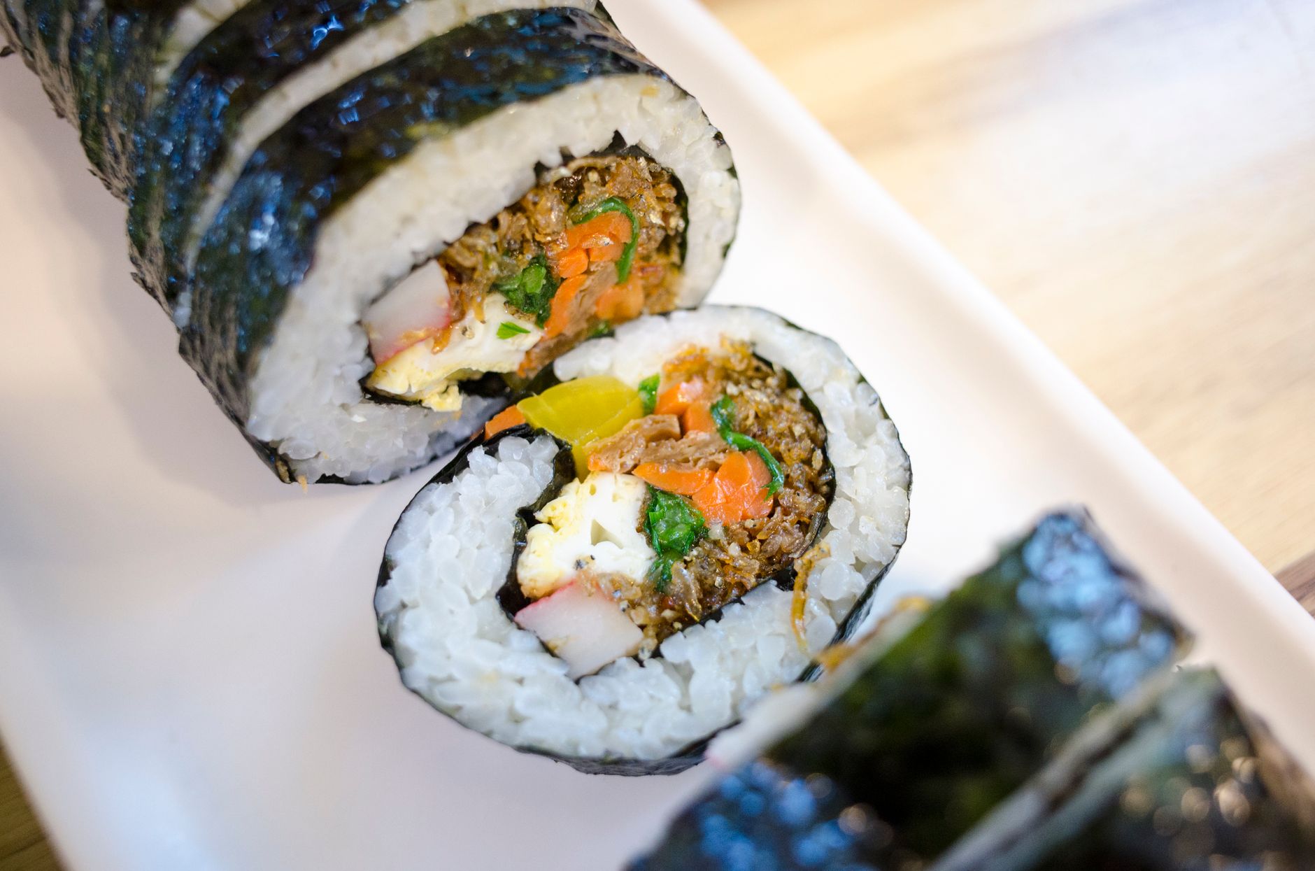 Close-up view of Korean gimbap sushi rolls with vegetables and seafood on a ceramic plate.