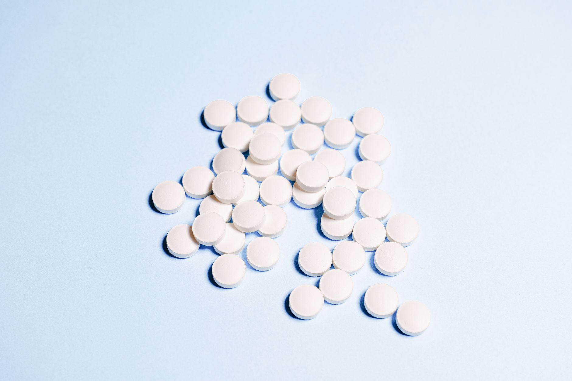 A collection of white tablets scattered on a light blue surface, perfect for health-related content.