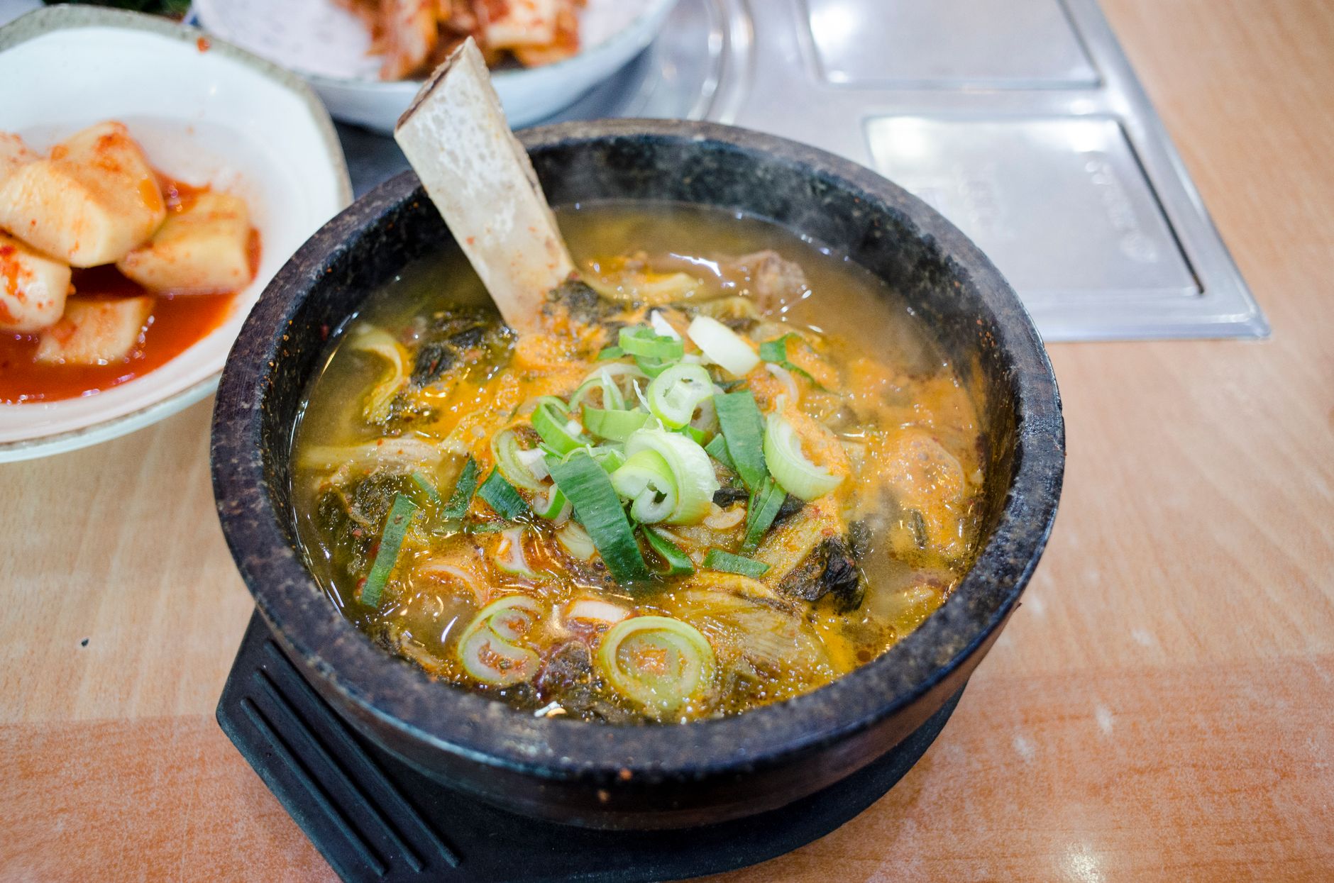Steamy hot stone bowl soup with fresh greens and side of kimchi, perfect for a cozy meal.
