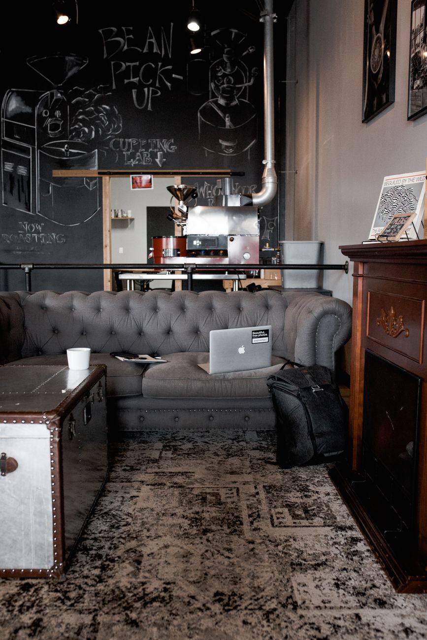 A stylish coffee shop scene featuring gray sofa, laptop, and vintage trunk with a fireplace in Greensboro, NC.