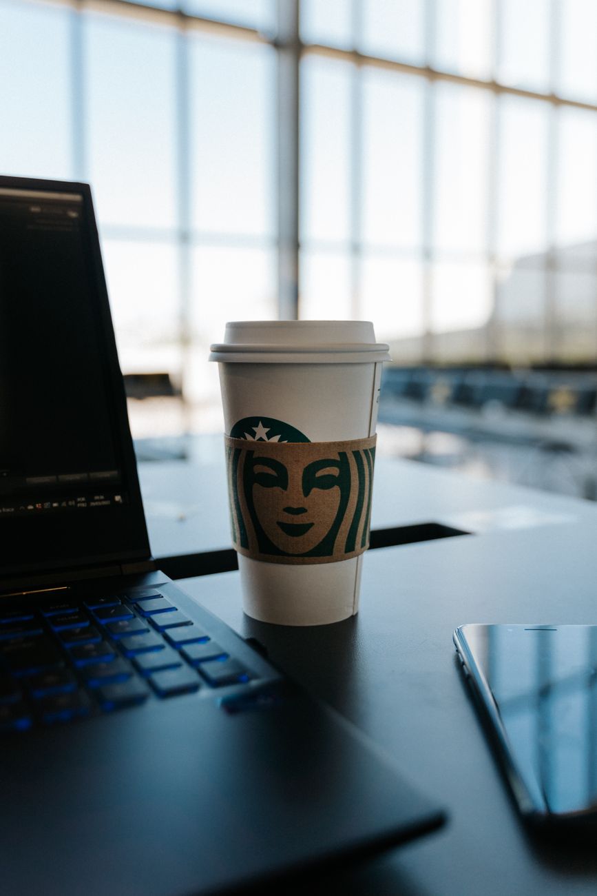 Disposable coffee cup on office table with laptop and phone nearby, in a bright workspace environment.