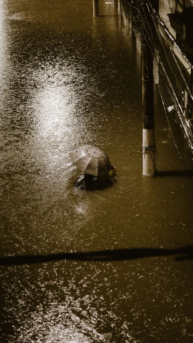 A person with an umbrella navigates a flooded street in Rio de Janeiro during heavy rain at night.