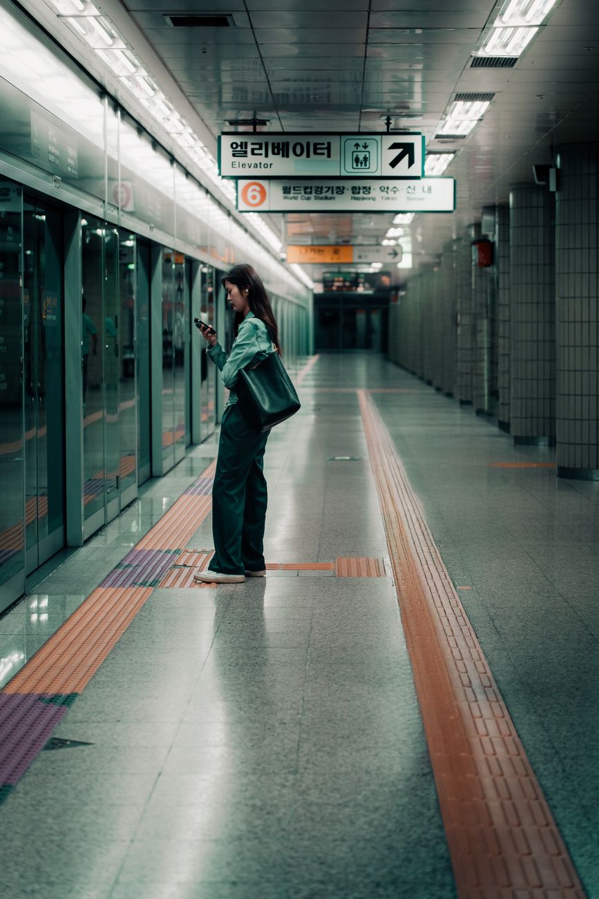 A woman standing alone, checking her phone in a Seoul subway station.