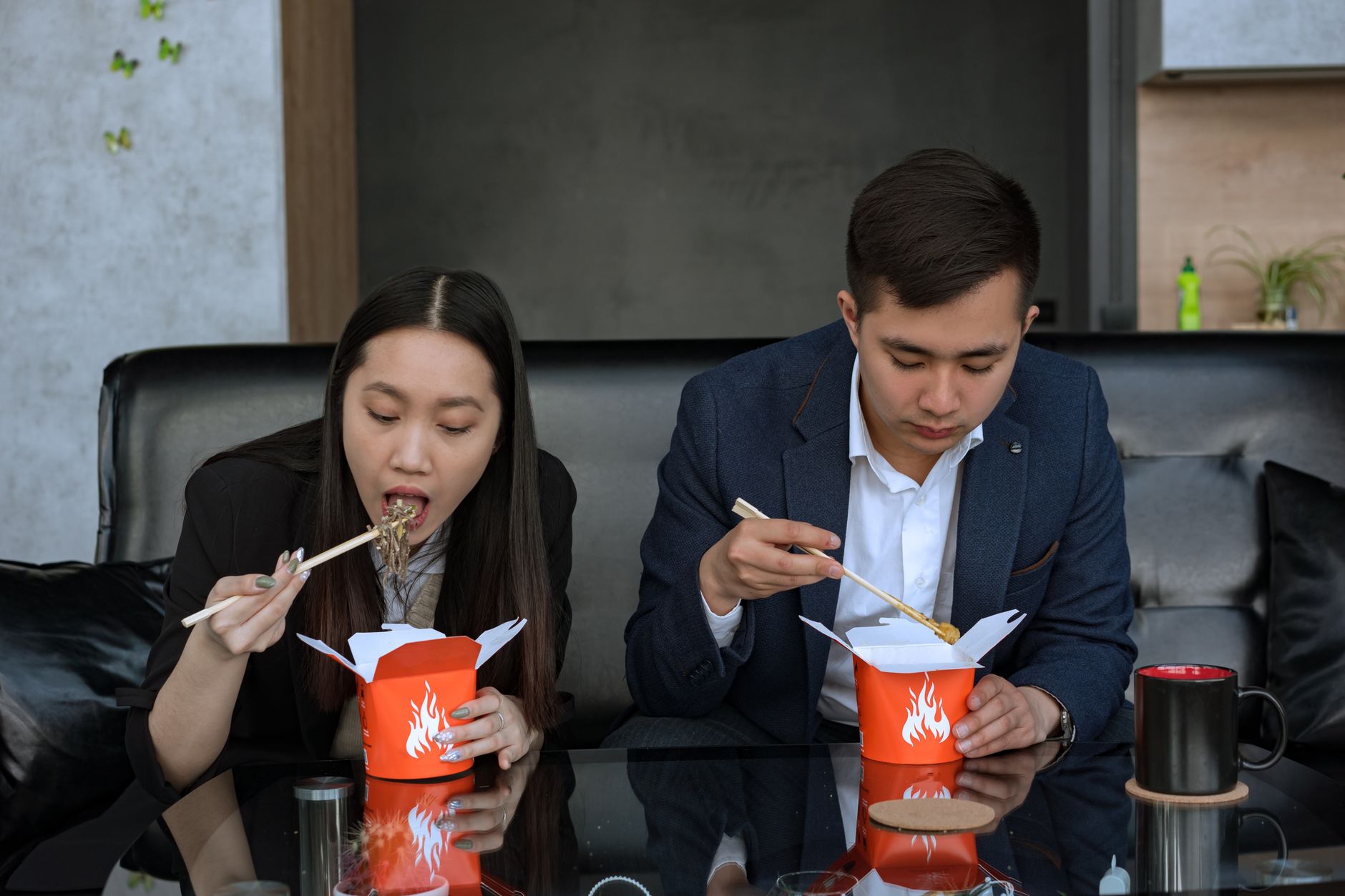 Two colleagues in an office setting enjoying Asian takeaway noodles during their lunch break.