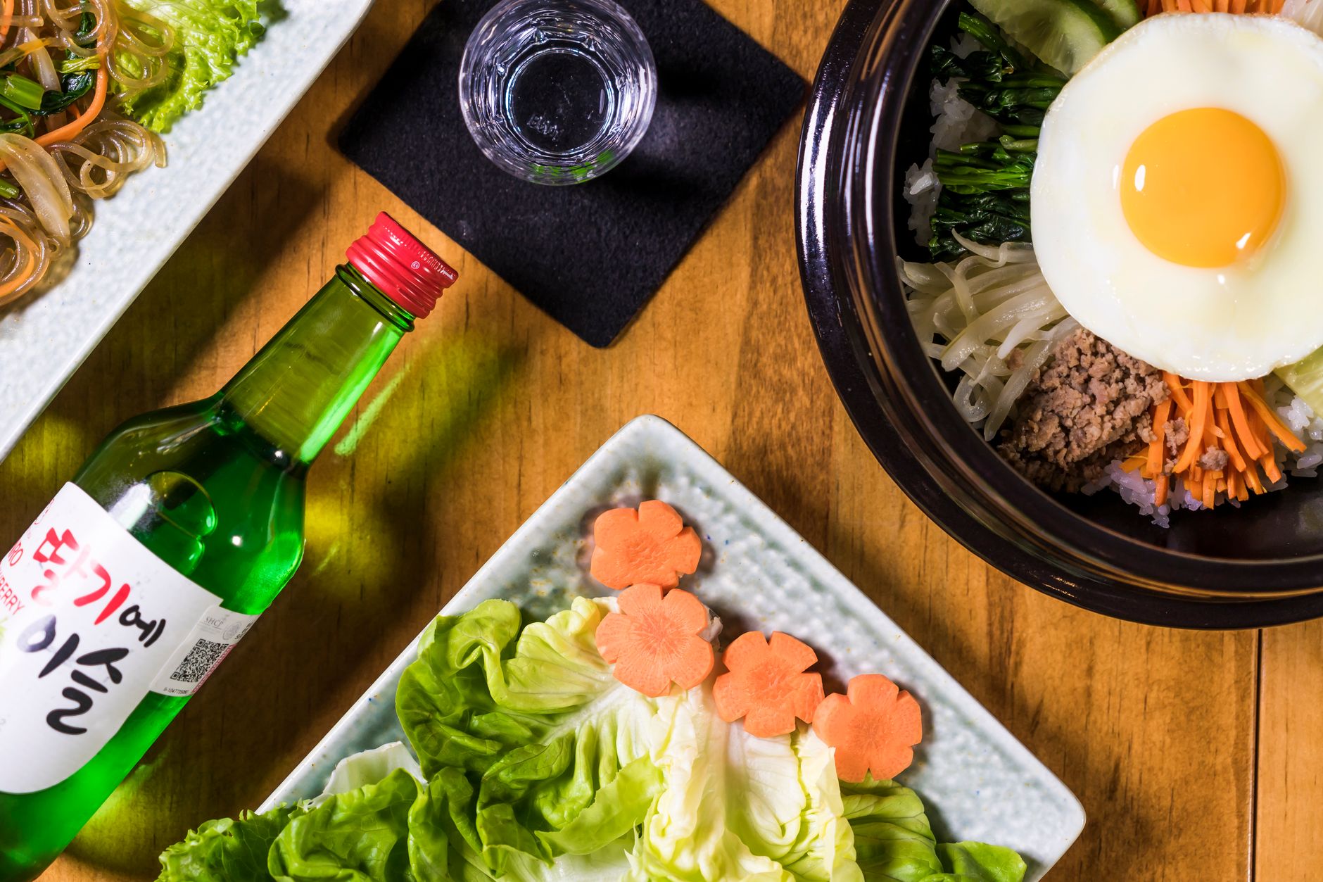 A colorful display of Korean bibimbap with soju, showcasing vibrant ingredients and food styling.