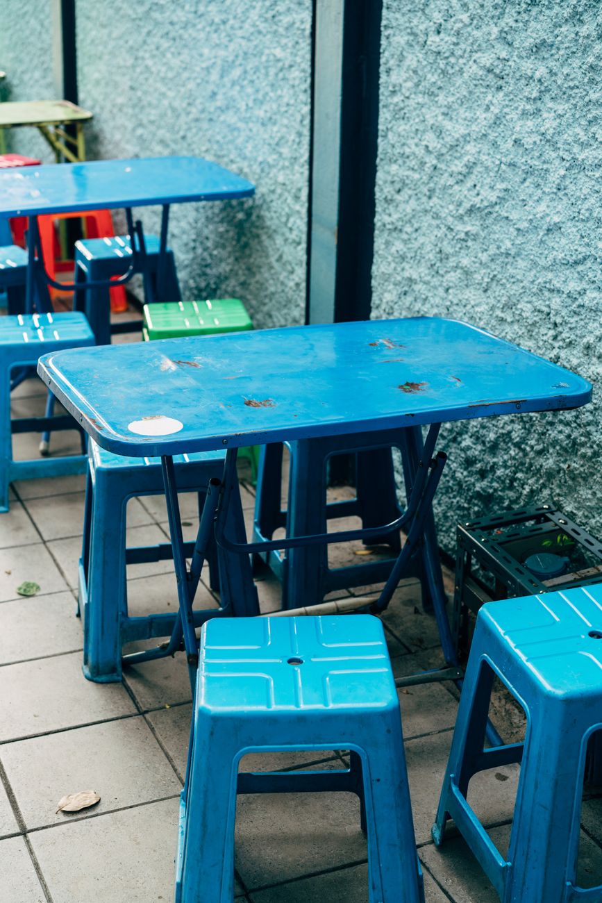 Bright blue plastic tables and stools in an outdoor urban setting, perfect for casual dining.