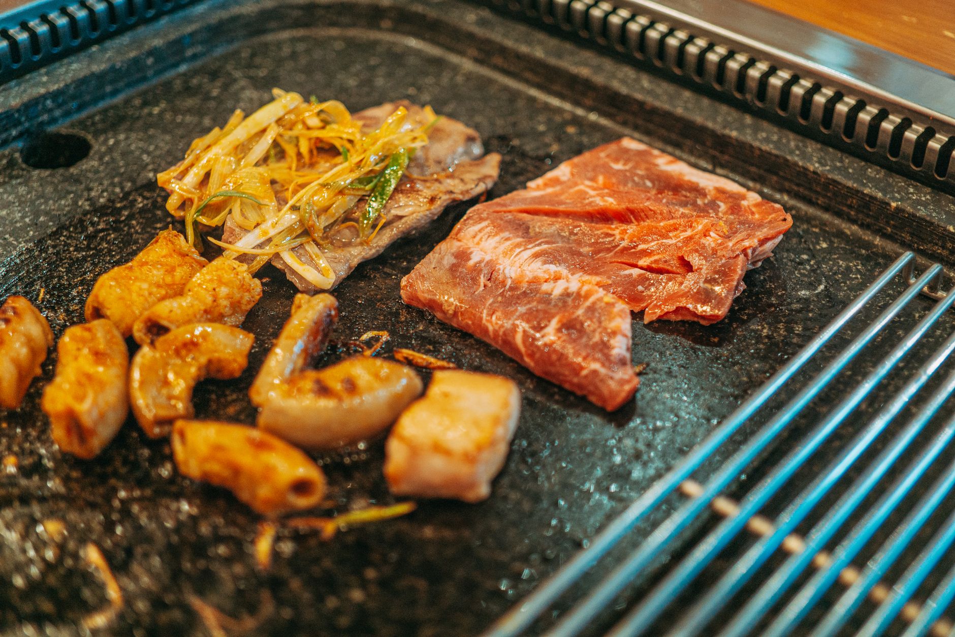Close-up of assorted meats and vegetables cooking on a Korean barbecue grill.