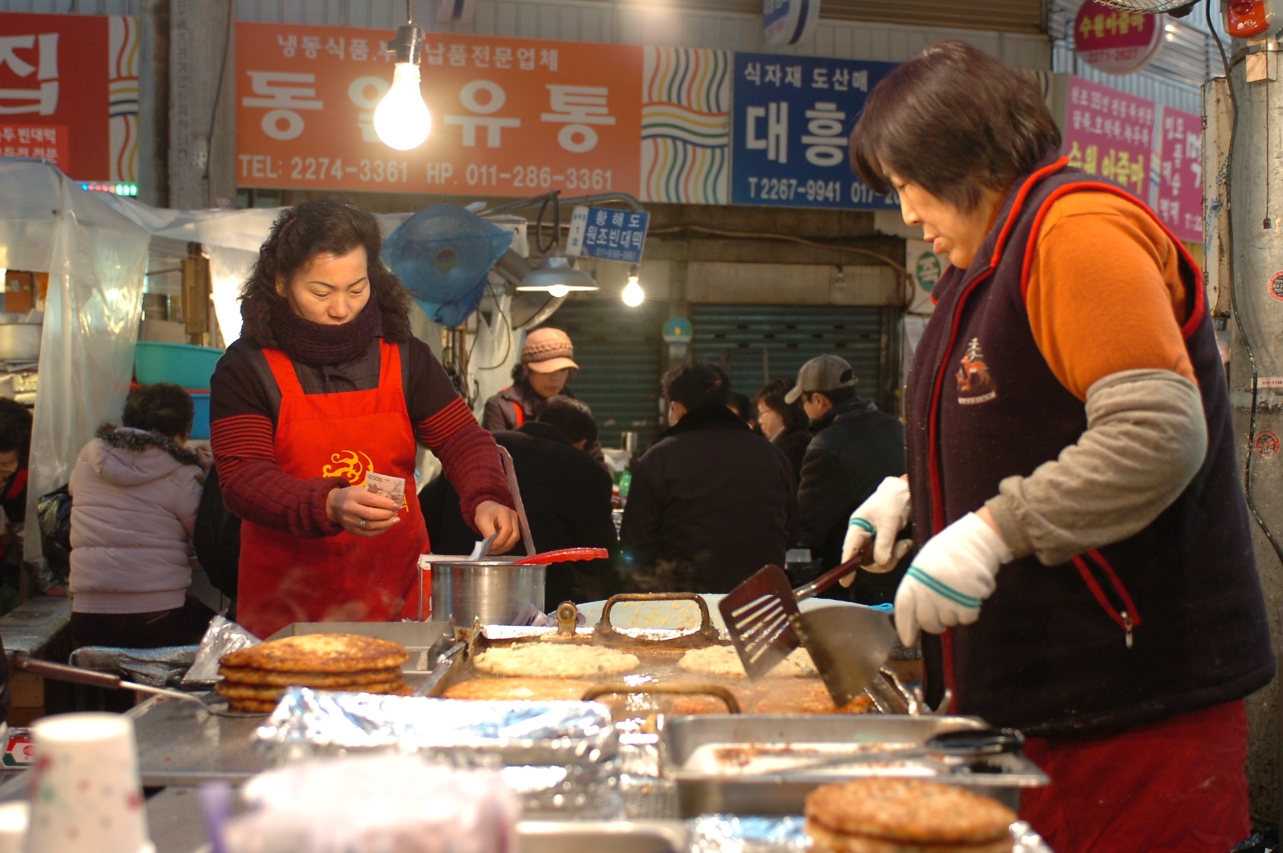 Ajummas (term referring to married women) fry bindaetteok (Korean mung bean pancakes) for customers at Gwangjang Market, Seoul, South Korea.