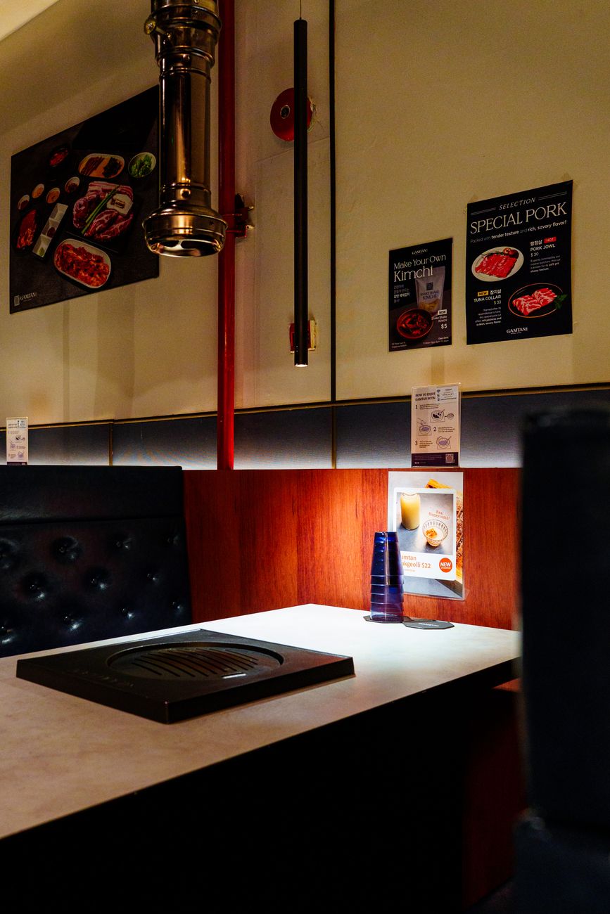 Empty Korean BBQ restaurant booth with grill and cozy lighting ambiance.