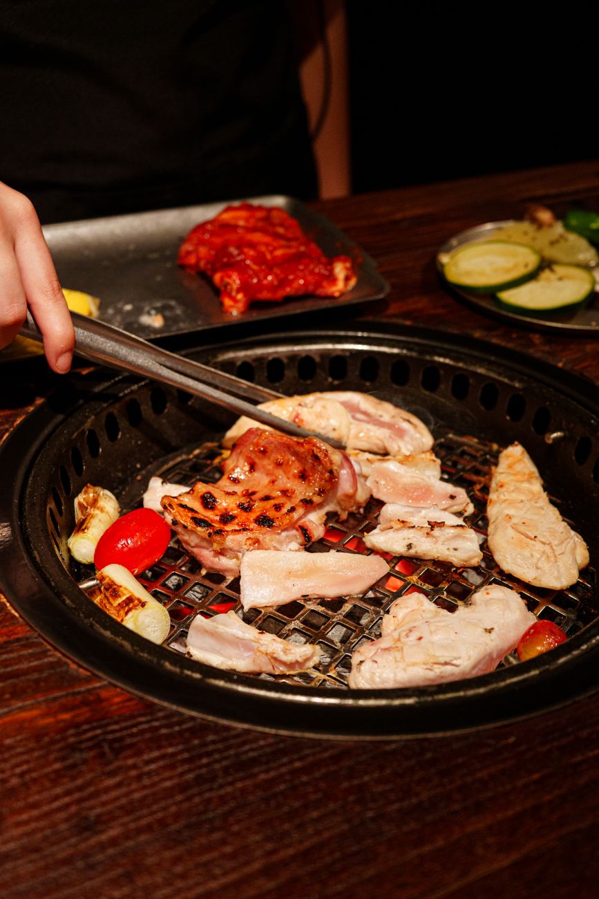 A variety of meats and vegetables being grilled on a Korean BBQ grill indoors, showcasing a vibrant culinary experience.